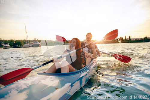 Image of Confident young couple kayaking on river together with sunset on the background