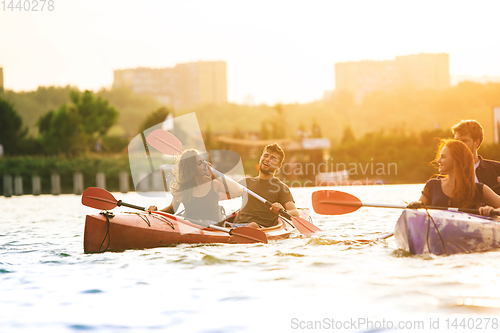 Image of Happy friends kayaking on river with sunset on the background