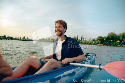 Image of Confident young man kayaking on river with sunset on the background