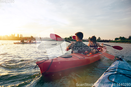 Image of Confident young couple kayaking on river together with sunset on the background