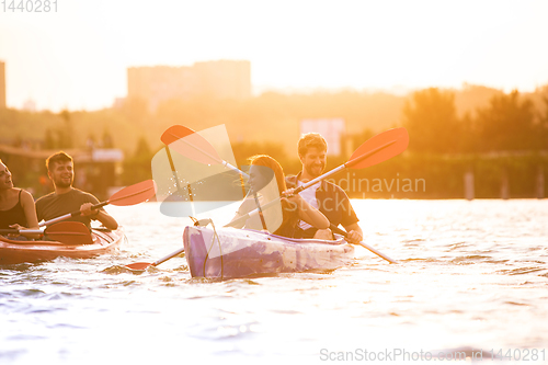 Image of Happy friends kayaking on river with sunset on the background