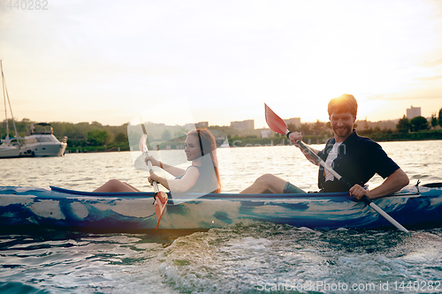 Image of Confident young couple kayaking on river together with sunset on the background