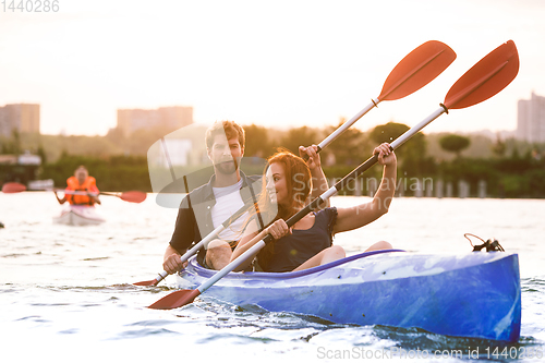 Image of Confident young couple kayaking on river together with sunset on the background