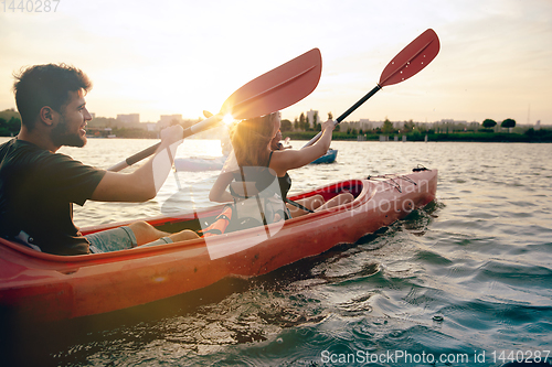 Image of Confident young couple kayaking on river together with sunset on the background