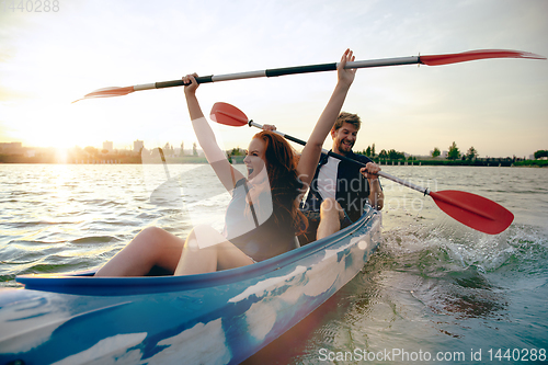 Image of Confident young couple kayaking on river together with sunset on the background