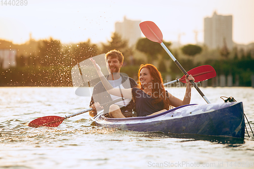 Image of Confident young couple kayaking on river together with sunset on the background