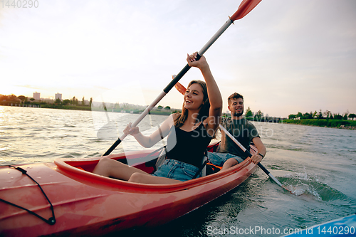 Image of Confident young couple kayaking on river together with sunset on the background