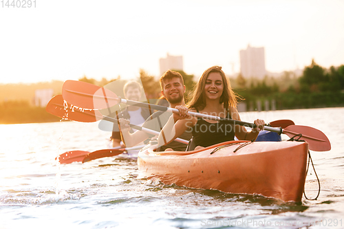 Image of Happy friends kayaking on river with sunset on the background