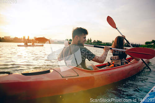 Image of Confident young couple kayaking on river together with sunset on the background