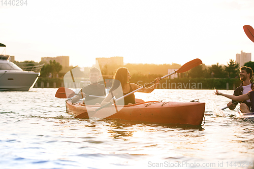 Image of Happy friends kayaking on river with sunset on the background