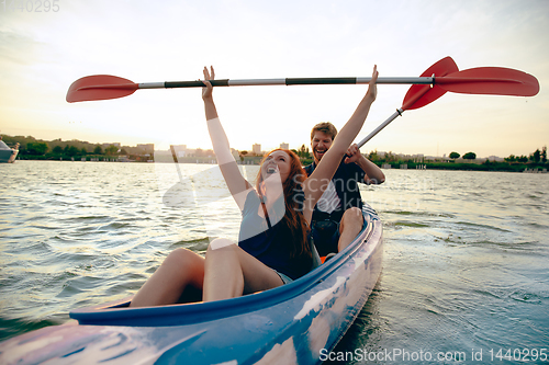 Image of Confident young couple kayaking on river together with sunset on the background