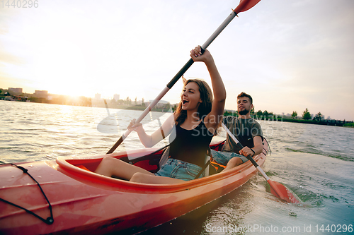 Image of Confident young couple kayaking on river together with sunset on the background