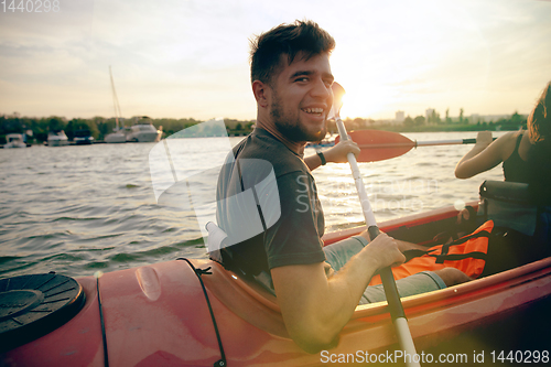 Image of Confident young couple kayaking on river together with sunset on the background