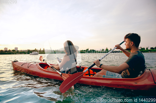 Image of Confident young couple kayaking on river together with sunset on the background