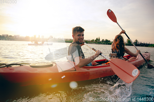 Image of Confident young couple kayaking on river together with sunset on the background