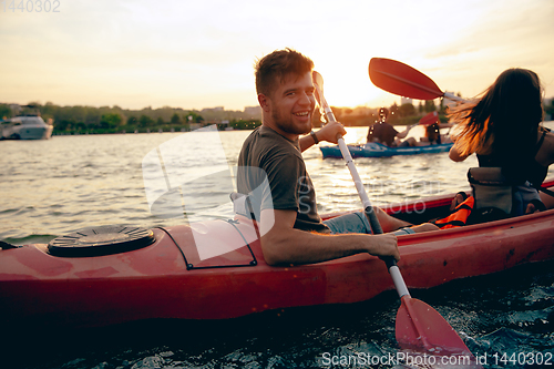 Image of Confident young couple kayaking on river together with sunset on the background