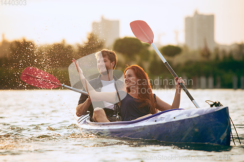 Image of Confident young couple kayaking on river together with sunset on the background