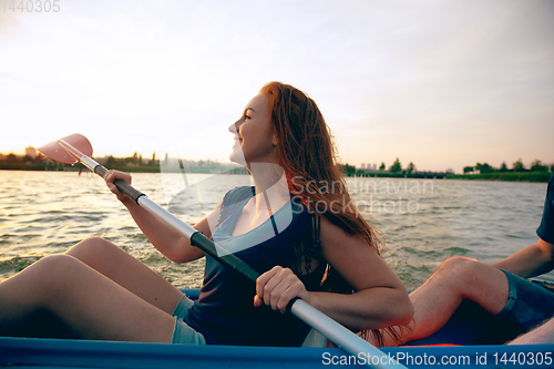 Image of Confident young woman kayaking on river with sunset on the background