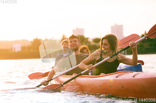 Image of Happy friends kayaking on river with sunset on the background