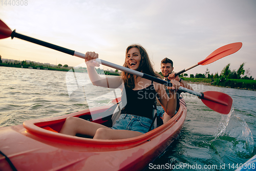 Image of Confident young couple kayaking on river together with sunset on the background