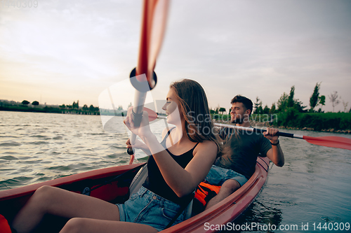 Image of Confident young couple kayaking on river together with sunset on the background