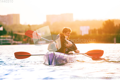 Image of Confident young couple kayaking on river together with sunset on the background