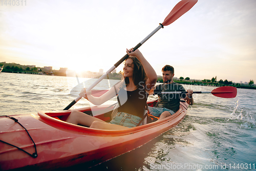 Image of Confident young couple kayaking on river together with sunset on the background