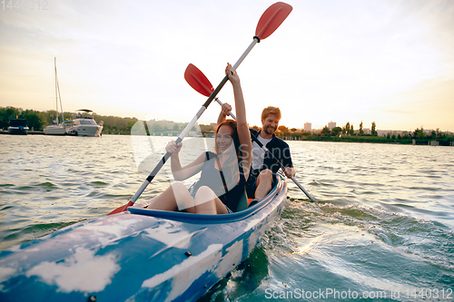 Image of Confident young couple kayaking on river together with sunset on the background