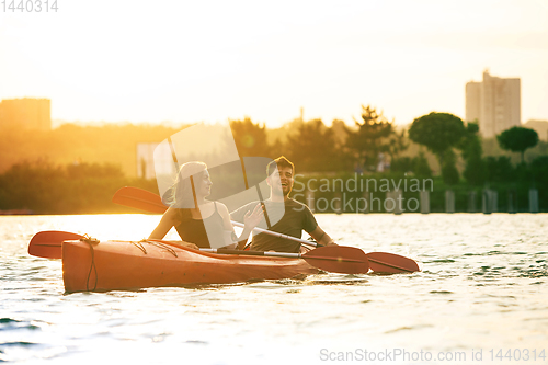 Image of Confident young couple kayaking on river together with sunset on the background