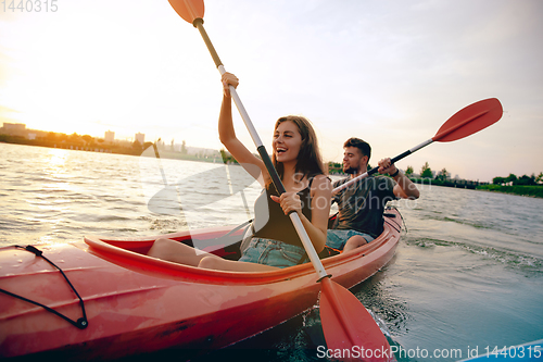 Image of Confident young couple kayaking on river together with sunset on the background