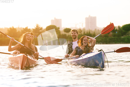 Image of Happy friends kayaking on river with sunset on the background