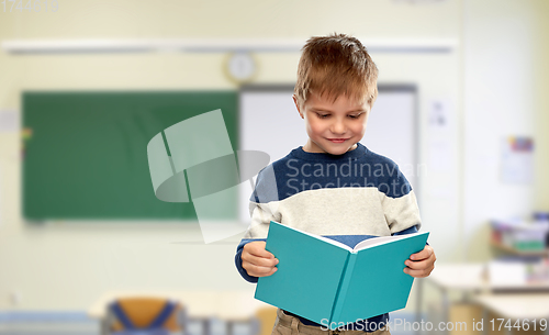 Image of smiling little boy reading book at school