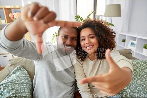 Image of happy couple making selfie frame gesture at home