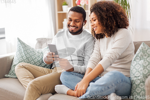 Image of happy couple with smartphone and earphones at home