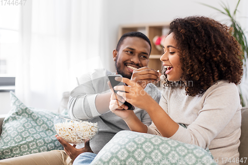 Image of african couple with popcorn and smartphone at home