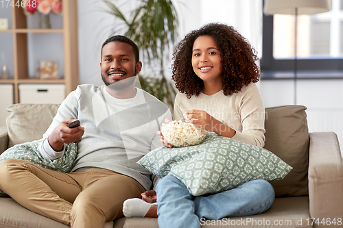 Image of african couple with popcorn watching tv at home