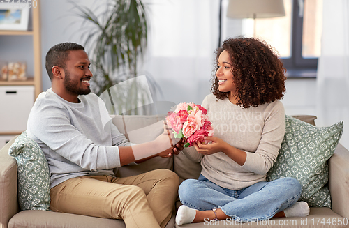 Image of happy couple with bunch of flowers at home