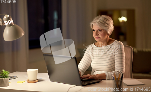 Image of senior woman with laptop at home in evening