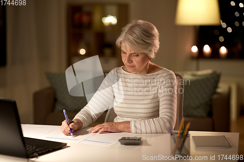 Image of senior woman filling tax form at home in evening