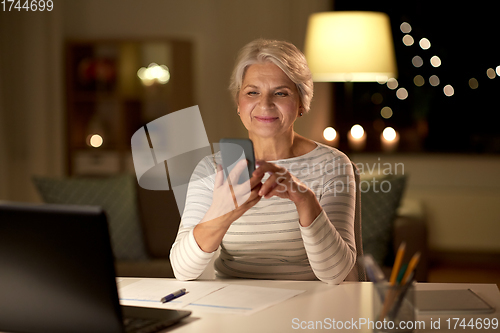 Image of senior woman with smartphone at home at night