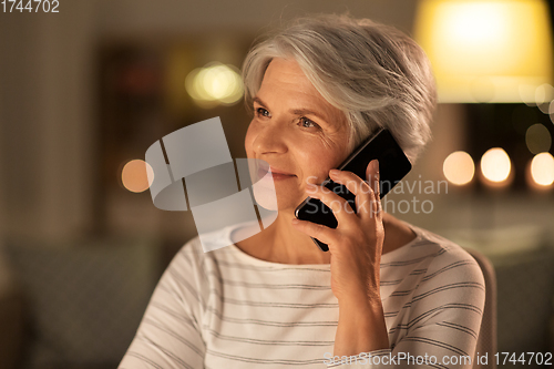 Image of old woman calling on smartphone at home in evening