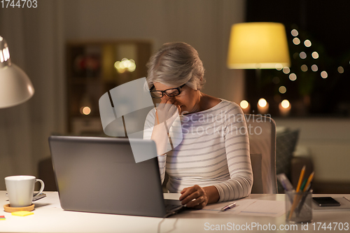 Image of tired senior woman with laptop at home at night