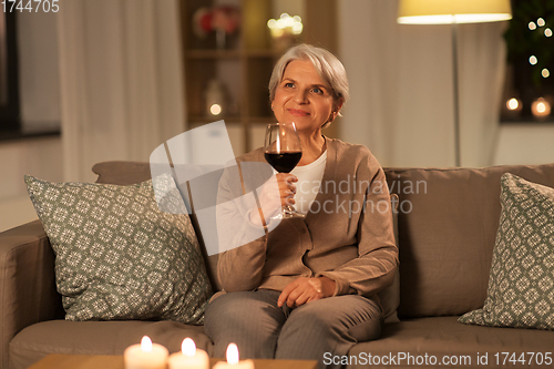 Image of senior woman drinking red wine at home in evening