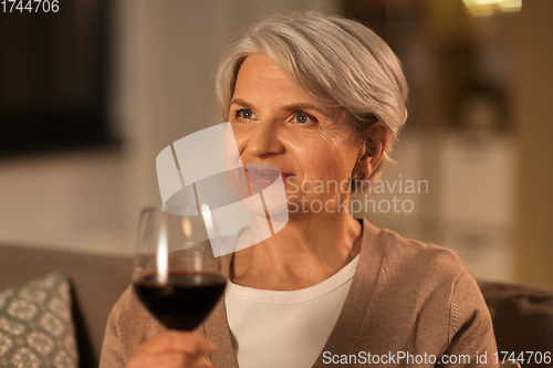 Image of senior woman drinking red wine at home in evening