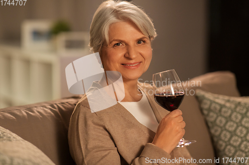 Image of senior woman drinking red wine at home in evening