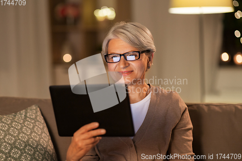 Image of happy senior woman with tablet pc at home at night