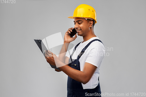 Image of indian builder with clipboard calling on cellphone