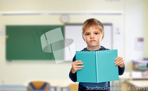 Image of displeased little boy with book at school
