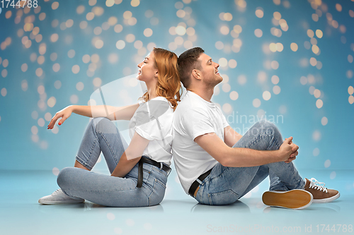 Image of happy couple in white t-shirts sitting on floor