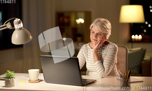 Image of senior woman with laptop at home in evening